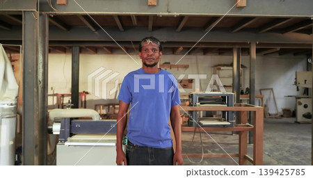 Standing carpenter wearing safety glasses holding tape measure in woodworking workshop with planer 139425785