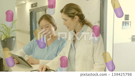 Discussing nurse and physician reviewing tablet at hospital reception, floating capsule graphics Discussing nurse and physician reviewing tablet at hospital reception, floating capsule graphics 139425798