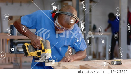 Carpenter wearing goggles cutting wooden plank in workshop, with yellow jigsaw and digital icons Carpenter wearing goggles cutting wooden plank in workshop, with yellow jigsaw and digital icons 139425811