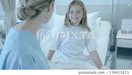 Smiling child in hospital gown talking with nurse in scrubs by hospital bed, with IV stand 139425813