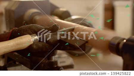 Shaping wooden spindle blank on lathe at workshop, guiding chisel and scattering wood shavings Shaping wooden spindle blank on lathe at workshop, guiding chisel and scattering wood shavings 139425822