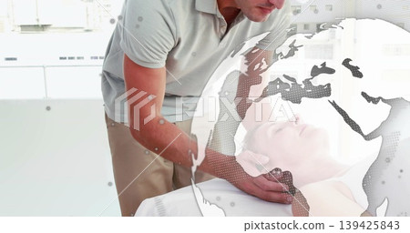 Leaning therapist supporting patient head treating neck on table in clinic, with world map overlay Leaning therapist supporting patient head treating neck on table in clinic, with world map overlay 139425843