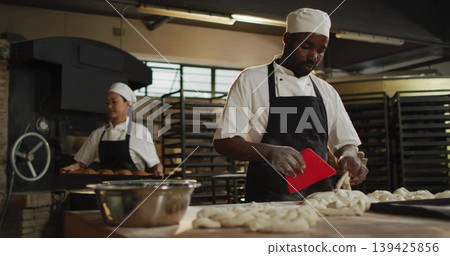 Shaping braided loaves baker wearing chef uniform at bakery kitchen, with dough scraper, copy space 139425856