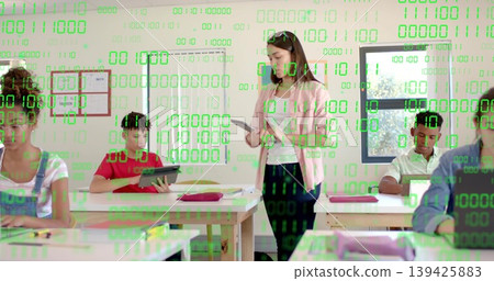 Holding tablet teacher by desk in classroom, students tapping tablets under green binary overlay 139425883