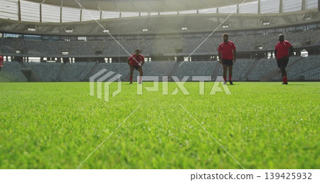 Standing five rugby players wearing red jerseys black shorts on grass pitch under roof with seating Standing five rugby players wearing red jerseys black shorts on grass pitch under roof with seating 139425932