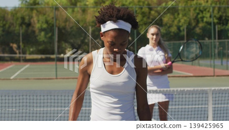Standing adult African American female tennis player scanning court, with tennis net Standing adult African American female tennis player scanning court, with tennis net 139425965