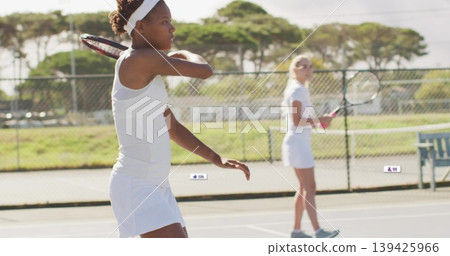 Practicing backhand swing woman in white tennis attire on court with rackets, fence, copy space Practicing backhand swing woman in white tennis attire on court with rackets, fence, copy space 139425966