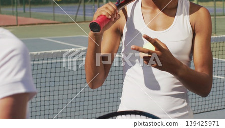 Signaling female tennis player holding racket near net on outdoor court, with fence and court lines Signaling female tennis player holding racket near net on outdoor court, with fence and court lines 139425971