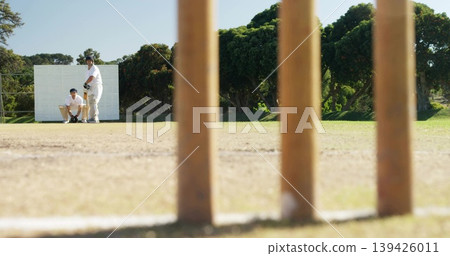 Framing wooden stumps occupying center at pitch, batter in pads helmet holding bat, keeper gloving Framing wooden stumps occupying center at pitch, batter in pads helmet holding bat, keeper gloving 139426011