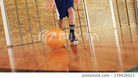 Dribbling teenage male handling basketball on shiny gym court, showing maroon sneakers reflection Dribbling teenage male handling basketball on shiny gym court, showing maroon sneakers reflection 139426021