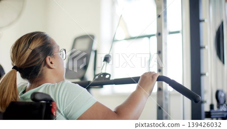 Gripping woman in wheelchair wearing mint tee and glasses using lat pulldown at gym, copy space Gripping woman in wheelchair wearing mint tee and glasses using lat pulldown at gym, copy space 139426032