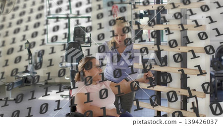 Helping trainer guiding client in wheelchair wearing pink reaching bars at rehab gym binary digits Helping trainer guiding client in wheelchair wearing pink reaching bars at rehab gym binary digits 139426037