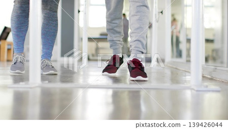 Walking two adults' lower legs through rehab with rails, mirror, striped leggings and sweatpants Walking two adults' lower legs through rehab with rails, mirror, striped leggings and sweatpants 139426044