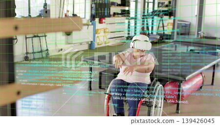 Reaching woman wearing white VR headset, seated in red wheelchair, using green grid in makerspace 139426045