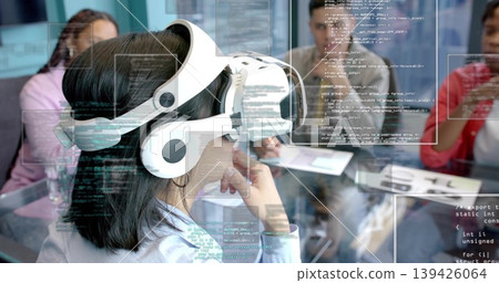 Wearing white headset, woman in blue shirt watching code at conference table, with laptop Wearing white headset, woman in blue shirt watching code at conference table, with laptop 139426064