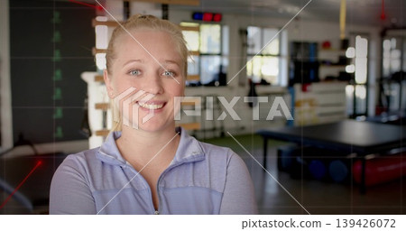 Smiling therapist wearing light purple jacket facing camera in rehab studio, with treatment table Smiling therapist wearing light purple jacket facing camera in rehab studio, with treatment table 139426072