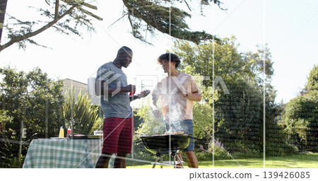 Grilling two men tending charcoal grill in yard holding sauce bottle and tongs near checked table Grilling two men tending charcoal grill in yard holding sauce bottle and tongs near checked table 139426085