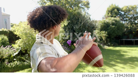 Preparing adult male in striped shirt holding football in backyard, purple Wi-Fi overlay Preparing adult male in striped shirt holding football in backyard, purple Wi-Fi overlay 139426088