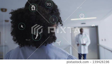 Standing woman in gown viewing approaching doctor in hospital corridor, with holographic icons 139426196