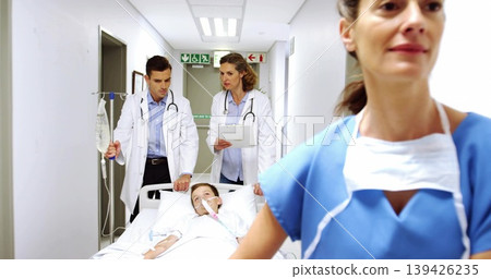 Rushing staff in scrubs and coats transporting child on gurney down hospital corridor with IV pole Rushing staff in scrubs and coats transporting child on gurney down hospital corridor with IV pole 139426235