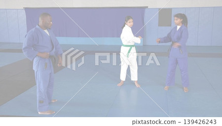 Directing instructor in blue gi guiding students sparring in dojo on foam mats, with colored belts Directing instructor in blue gi guiding students sparring in dojo on foam mats, with colored belts 139426243