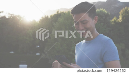 Smiling Asian man in light blue t-shirt holding smartphone on terrace, with coffee cup, copy space Smiling Asian man in light blue t-shirt holding smartphone on terrace, with coffee cup, copy space 139426262