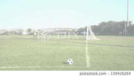 Walking uniformed soccer players heading toward goal net on park field, with ball resting in front Walking uniformed soccer players heading toward goal net on park field, with ball resting in front 139426264