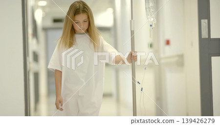 Walking gowned child holding IV pole through hospital hallway with corridor doors and wristband 139426279