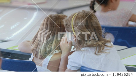 Whispering blonde schoolgirl leaning close at blue classroom desk with notebooks, paper and pencils Whispering blonde schoolgirl leaning close at blue classroom desk with notebooks, paper and pencils 139426294