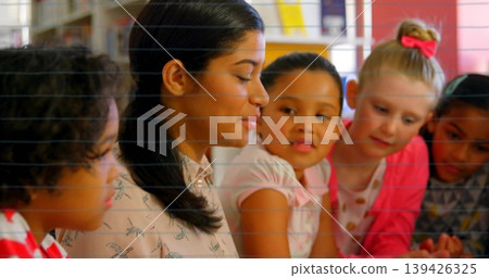 Teacher guiding reading session in classroom library, with table, bookshelves and books, copy space Teacher guiding reading session in classroom library, with table, bookshelves and books, copy space 139426325