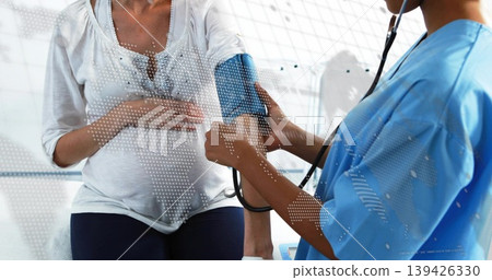 Nurse in scrubs wrapping blood pressure cuff around pregnant patient on exam bench, map overlay 139426330