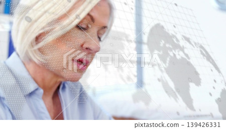 Reviewing data, senior woman wearing light blue blouse in office with world map overlay, copy space Reviewing data, senior woman wearing light blue blouse in office with world map overlay, copy space 139426331