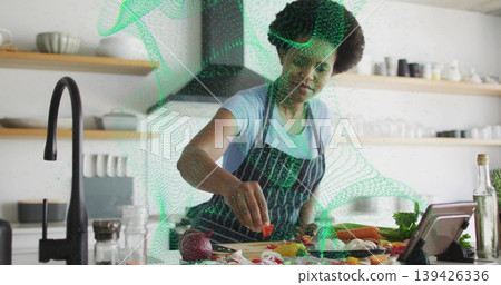 Home cook slicing vegetables on cutting board at kitchen island, with tablet and egg shells Home cook slicing vegetables on cutting board at kitchen island, with tablet and egg shells 139426336