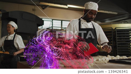 Kneading male chef dividing dough inside bakery kitchen, with red bench scraper and baking racks 139426341