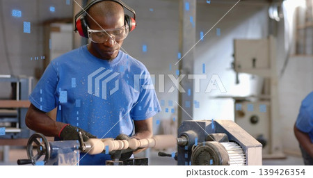 Operating lathe, mature Black man shaping spindle with shavings in shop, wearing goggles and gloves Operating lathe, mature Black man shaping spindle with shavings in shop, wearing goggles and gloves 139426354