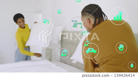 Couple arranging pillows on unmade bed with upholstered headboard in bedroom, with eco icons Couple arranging pillows on unmade bed with upholstered headboard in bedroom, with eco icons 139426414