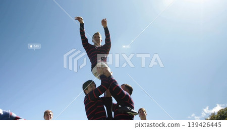Lifting rugby teammate during lineout wearing striped jerseys, beige shorts on grass under blue sky 139426445