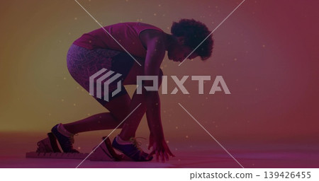 Sprinter crouching on starting block in studio, sporting tank top, patterned shorts and spikes Sprinter crouching on starting block in studio, sporting tank top, patterned shorts and spikes 139426455