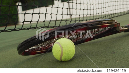 Displaying tennis racket and tennis ball on outdoor hard court, with taut tennis net background Displaying tennis racket and tennis ball on outdoor hard court, with taut tennis net background 139426459