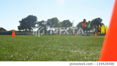 Training six soccer players practicing on pitch wearing bibs, with cones and dummies, copy space 139426486