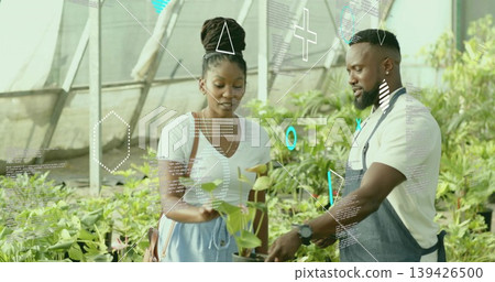 Examining customer and staff holding potted plant in greenhouse, with metal frame and apron Examining customer and staff holding potted plant in greenhouse, with metal frame and apron 139426500