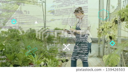 Holding tablet, horticultural workers monitoring potted plants in greenhouse, with data overlay 139426503