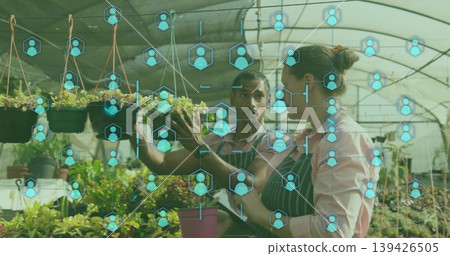 Plant caretakers wearing aprons examining hanging seedlings in greenhouse, with digital icons Plant caretakers wearing aprons examining hanging seedlings in greenhouse, with digital icons 139426505