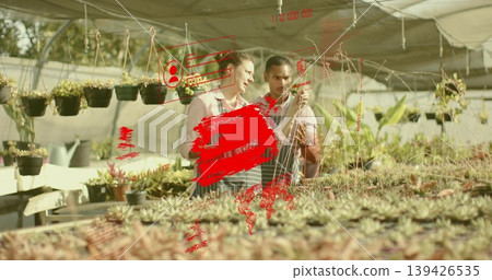 Two horticulturists wearing aprons inspecting succulent pots in greenhouse, with hanging planters Two horticulturists wearing aprons inspecting succulent pots in greenhouse, with hanging planters 139426535