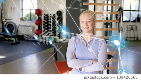 Standing woman in longsleeve top, crossing arms in studio with rack, network overlay, copy space Standing woman in longsleeve top, crossing arms in studio with rack, network overlay, copy space 139426563