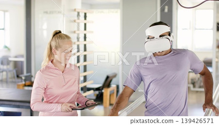 Walking patient purple tee VR headset using parallel bars rehab PT pink holding tablet, copy space Walking patient purple tee VR headset using parallel bars rehab PT pink holding tablet, copy space 139426571