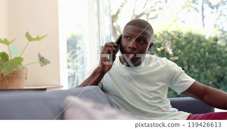 Holding phone, man wearing mint tee, maroon shorts sitting on sofa near sliding door with basket Holding phone, man wearing mint tee, maroon shorts sitting on sofa near sliding door with basket 139426613