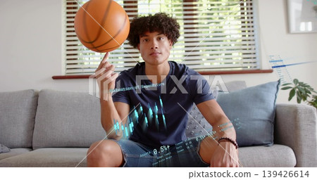 Spinning man wearing navy tee, denim shorts balancing basketball on sofa, with financial holograms Spinning man wearing navy tee, denim shorts balancing basketball on sofa, with financial holograms 139426614