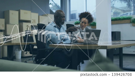Collaborating professionals in button-down and gray blazer pointing at laptop in modern office Collaborating professionals in button-down and gray blazer pointing at laptop in modern office 139426708