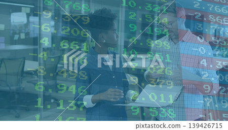Pointing pair in business casual viewing data on laptop at office with monitors desks chairs Pointing pair in business casual viewing data on laptop at office with monitors desks chairs 139426715